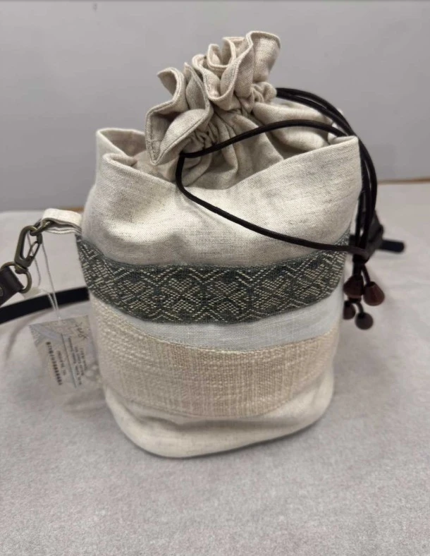 噶瑪蘭香蕉絲編織工藝束口袋以自然的米色棉麻材質為主體，搭配具有幾何紋路的傳統織帶裝飾