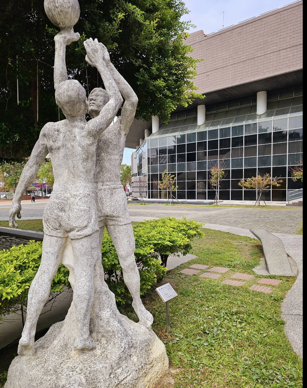 石雕作品描繪了兩位籃球員躍起、合力爭球與投籃的動態瞬間，展現了強烈的運動張力與生命力。